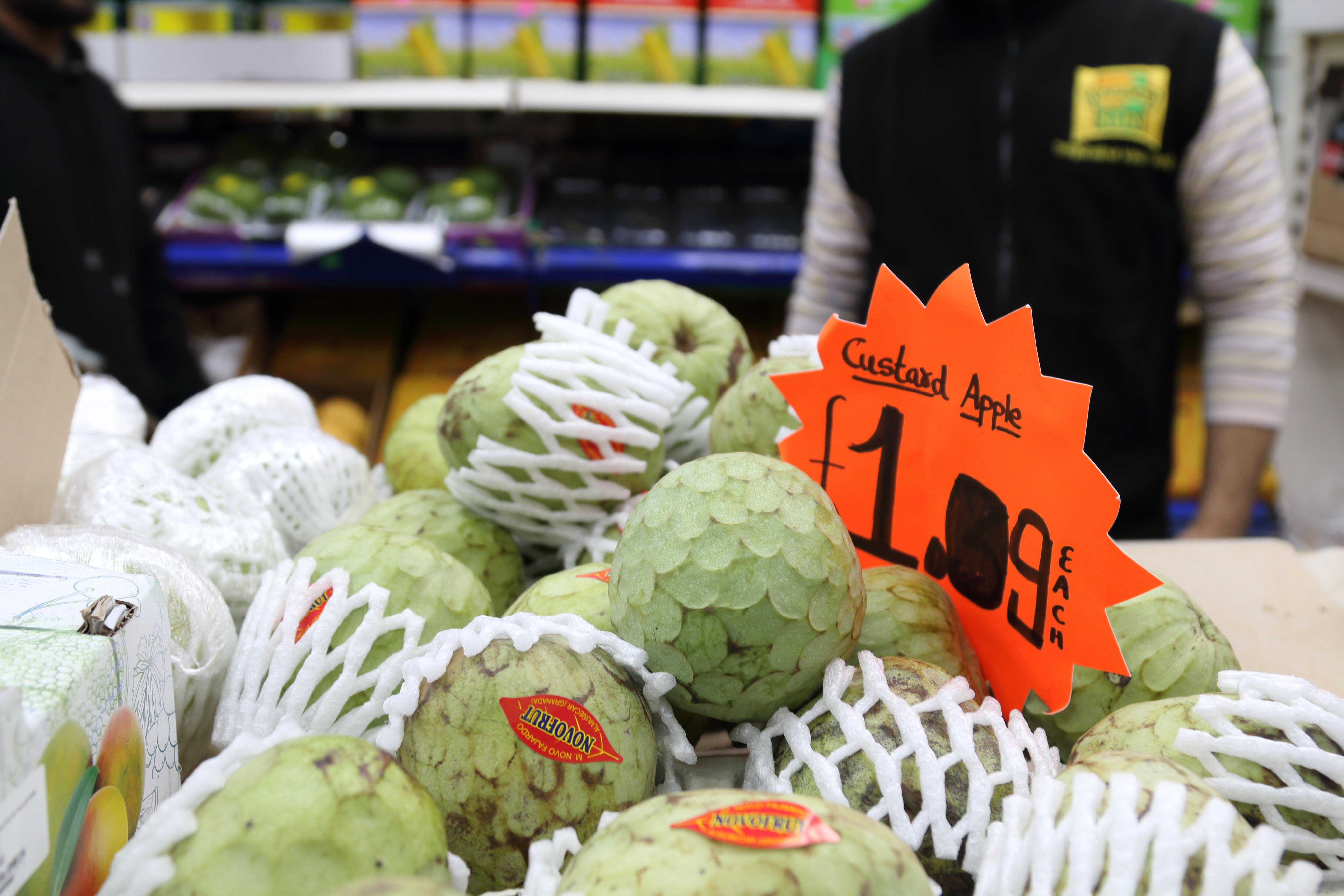 Inside Blue Mountain Peak grocery store, showing Custard Apples, round fruit with irregular green skins, packed in white polystyrene wrappers. A sign on orange card reads, ‘Custard Apple: £1.09 Each”.