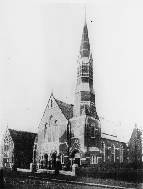 Black and white photograph of a large church with a large spire. A smaller church building can be seen to the left.
