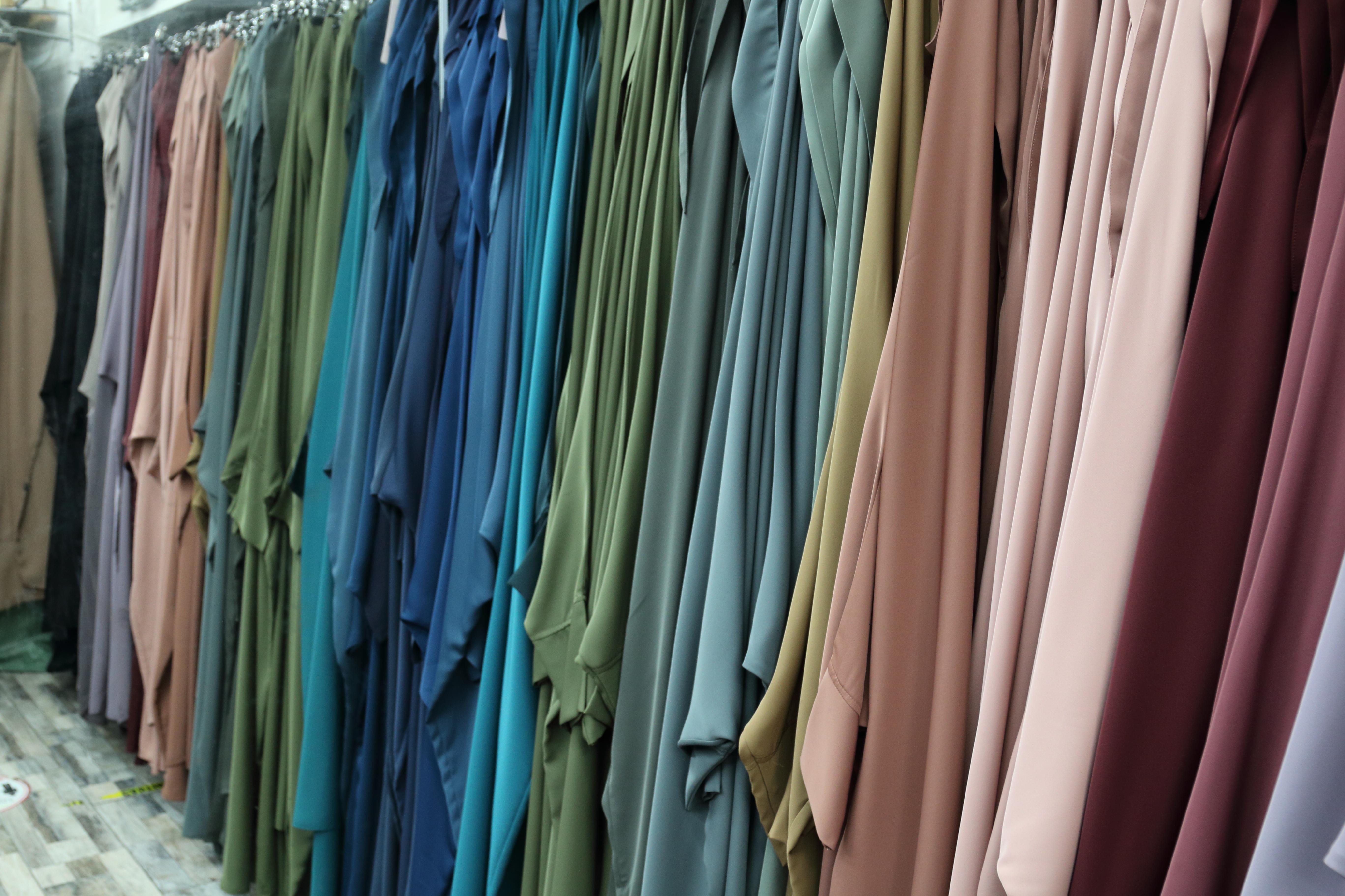Colour image showing Muslim modesty wear clothing in fine fabrics, in a variety of colours including blues, greens, greys, ochres, browns.