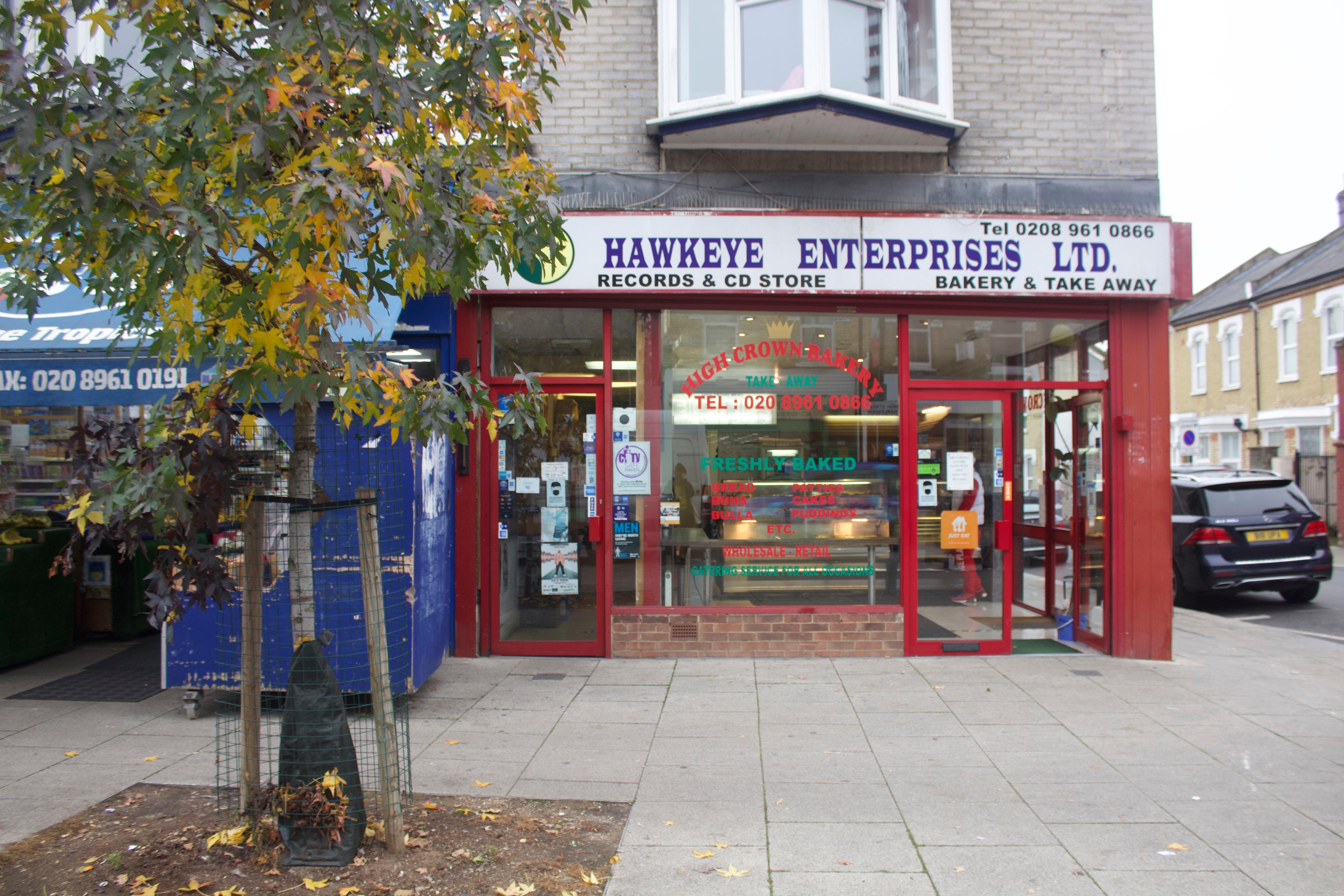 Shop front for Hawkeye Enterprises. The sign reads, ‘Hawkeye Enterprises Ltd: Records & CD Store; Bakery & Take away’.