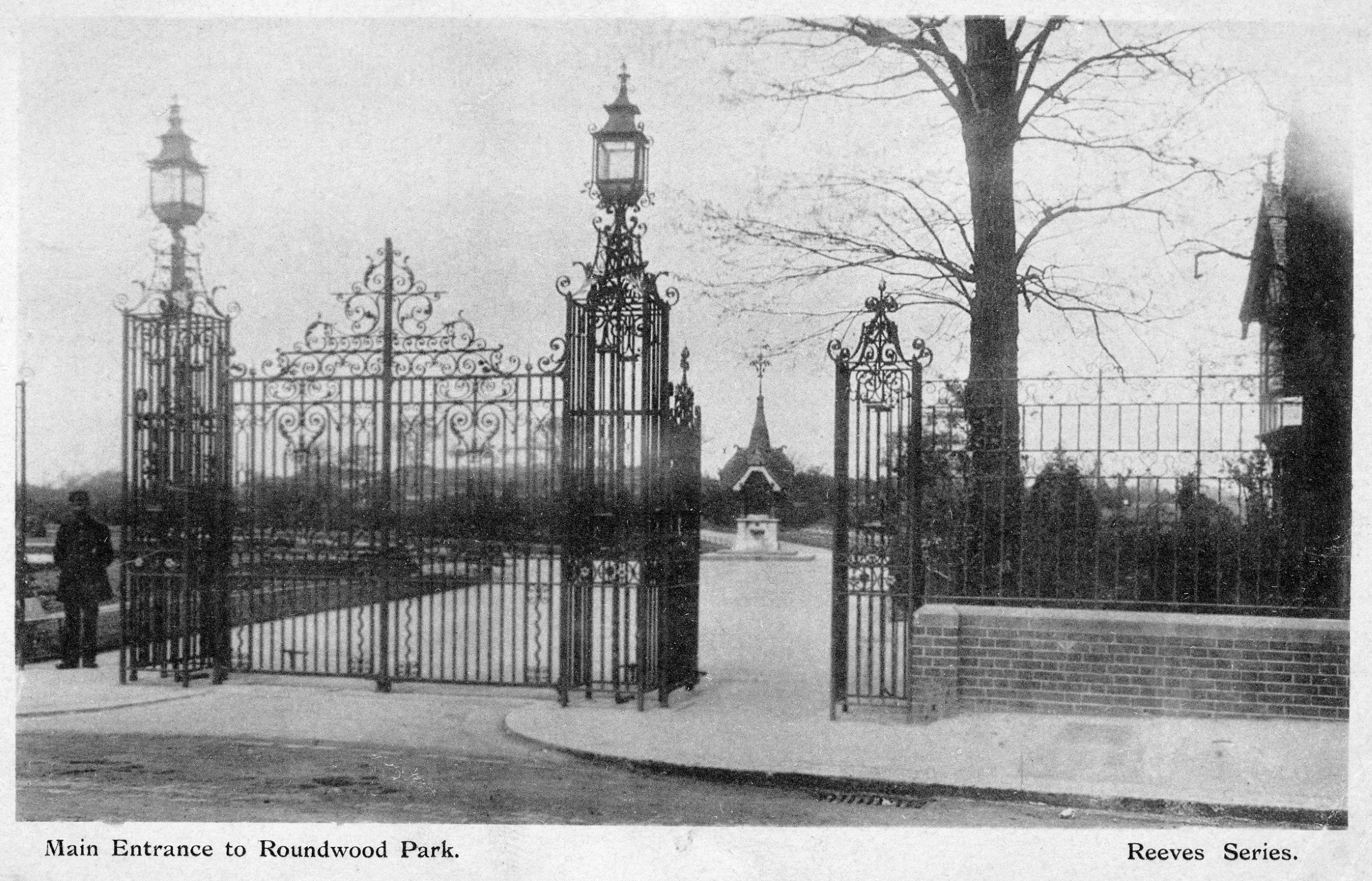 Postcard with black and white image showing gates at the entrance to a park. Underneath it is written, ‘Main Entrance to Roundwood Park’.
