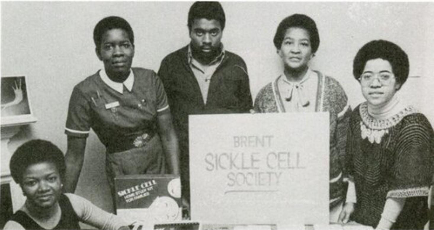 Black and white photograph showing five black people, with a sign reading, ‘Brent Sickle Cell Society’.